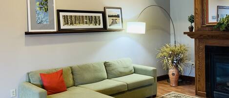 A living room with a sectional sofa, a patterned rug, a fireplace, and wall-mounted artwork.