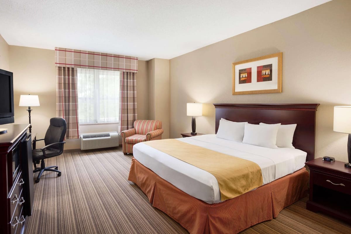 A hotel room with a large bed, two bedside tables, a desk with a chair, a television, and a window with curtains.