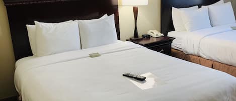 Habitación de hotel con dos camas, cada una con cabecero oscuro, ropa de cama blanca y un control remoto sobre la cama.