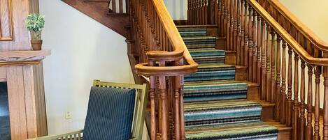 Una escalera de madera con barandilla, una silla con cojín y una alfombra estampada.