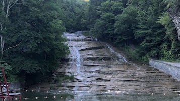A waterfall surrounded by dense forest, with a concrete viewing platform and safety railings.
