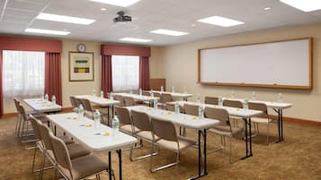 A conference room with multiple tables, chairs, a clock, a projector, and a whiteboard.