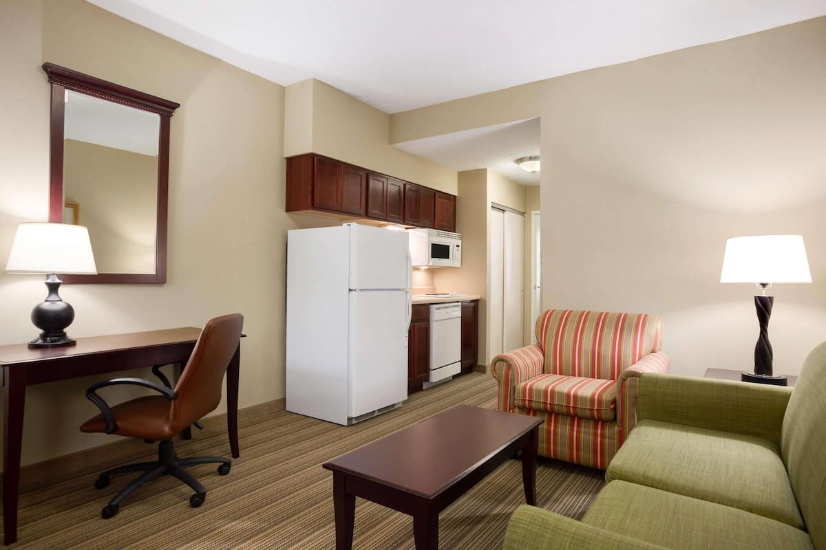 A compact hotel room with a kitchenette, a dining area, a sofa, and a desk with a chair.