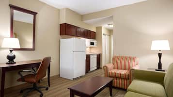 A compact hotel room with a kitchenette, a dining area, a sofa, and a desk with a chair.
