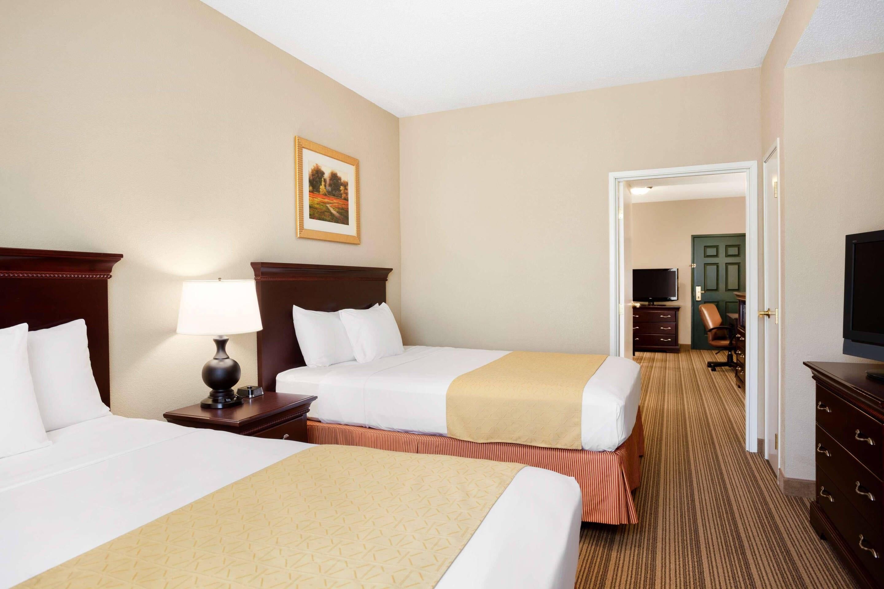 A hotel room with two beds, a desk, a chair, a television, and a door leading to another room.