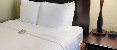Een hotelkamer met een net opgemaakt bed, een nachtkastje met een lamp en een klok.