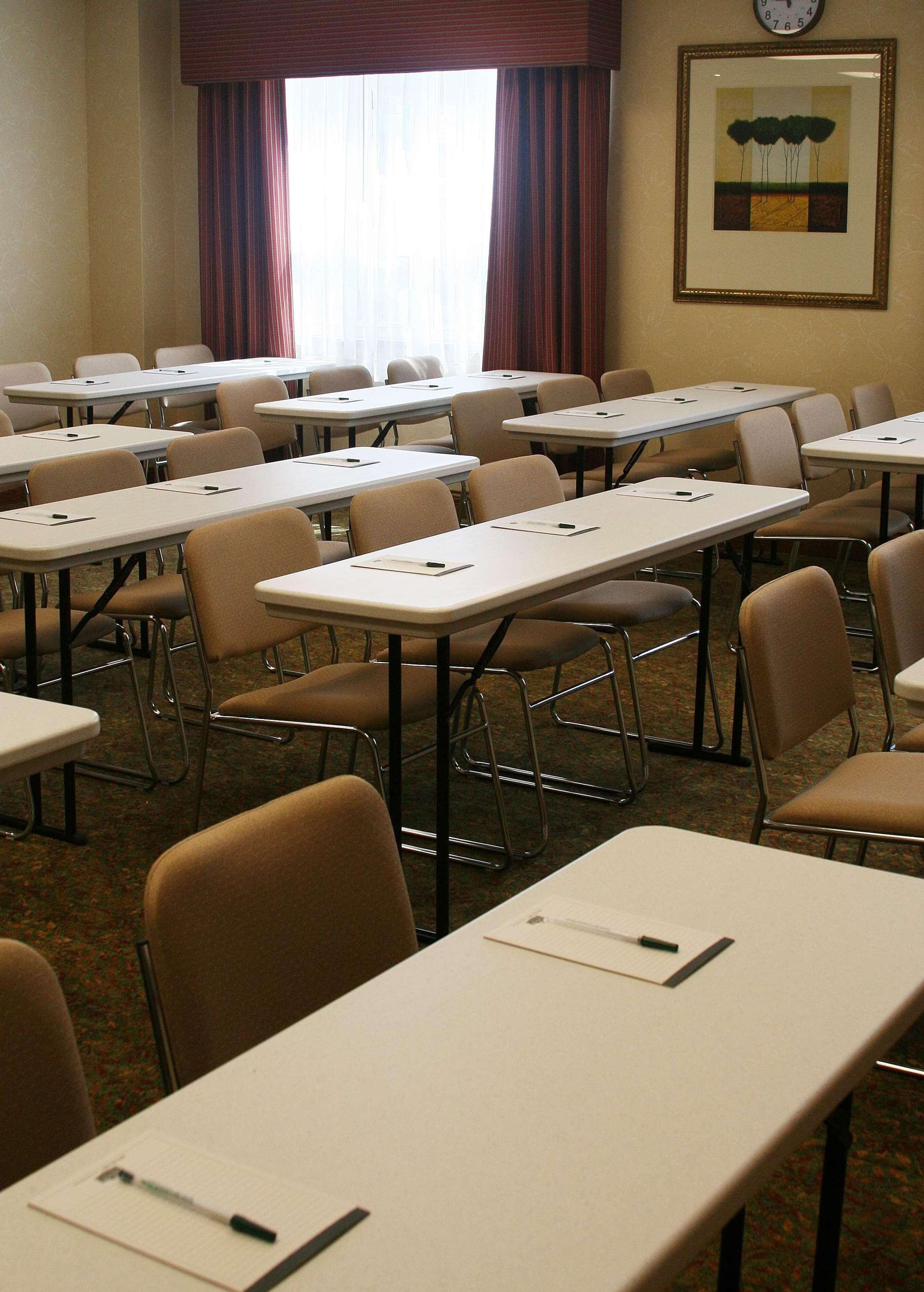 A conference room with multiple tables and chairs, a clock on the wall, and a framed picture above the tables.