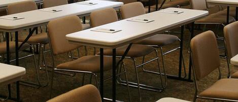 A conference room with multiple tables and chairs, a clock on the wall, and a framed picture above the tables.