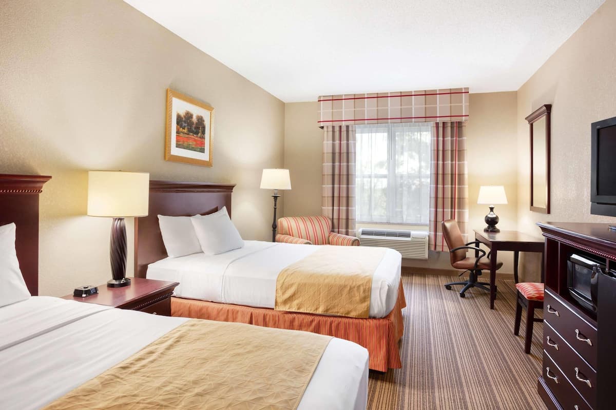 A hotel room with two beds, a desk, a chair, a television, and a window with curtains.