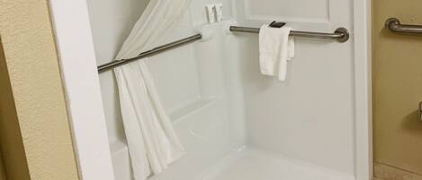 A walk-in shower with a glass door, a shower curtain, and a grab bar.