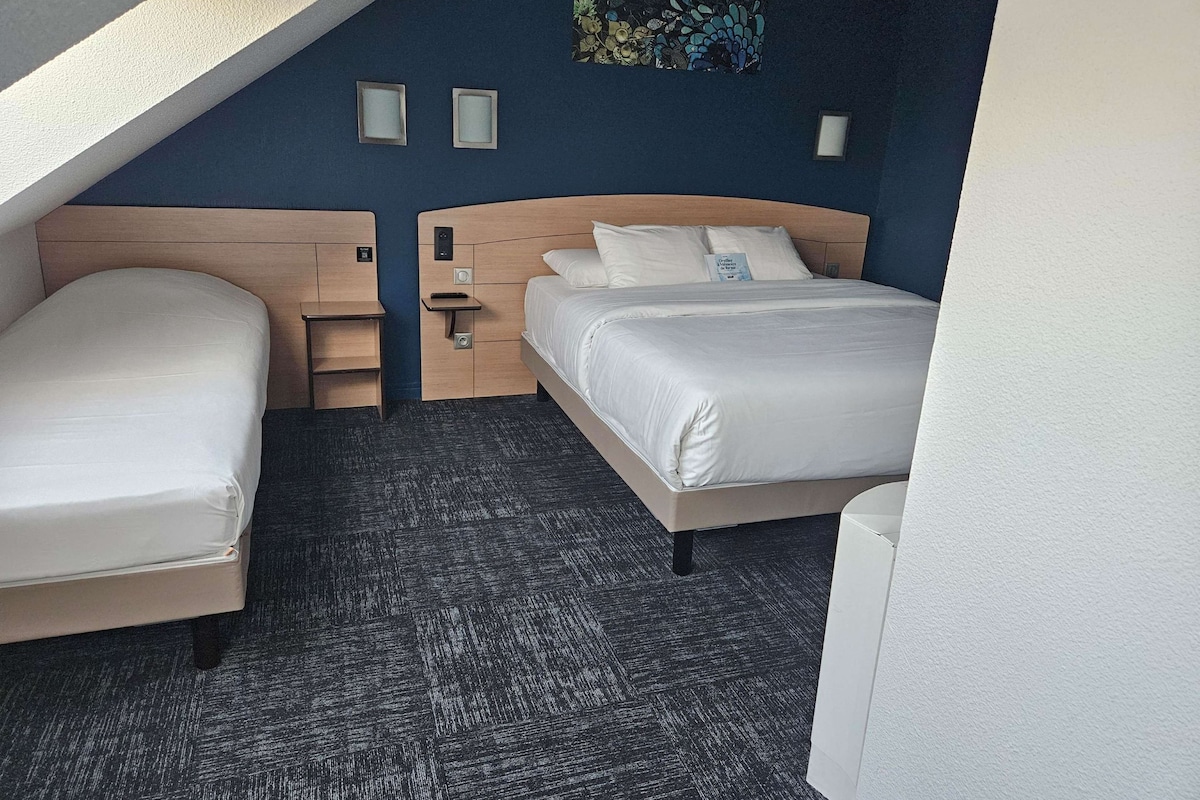 Habitación de hotel con dos camas, un cabecero de madera, una mesita pequeña y una obra de arte colgada en la pared.