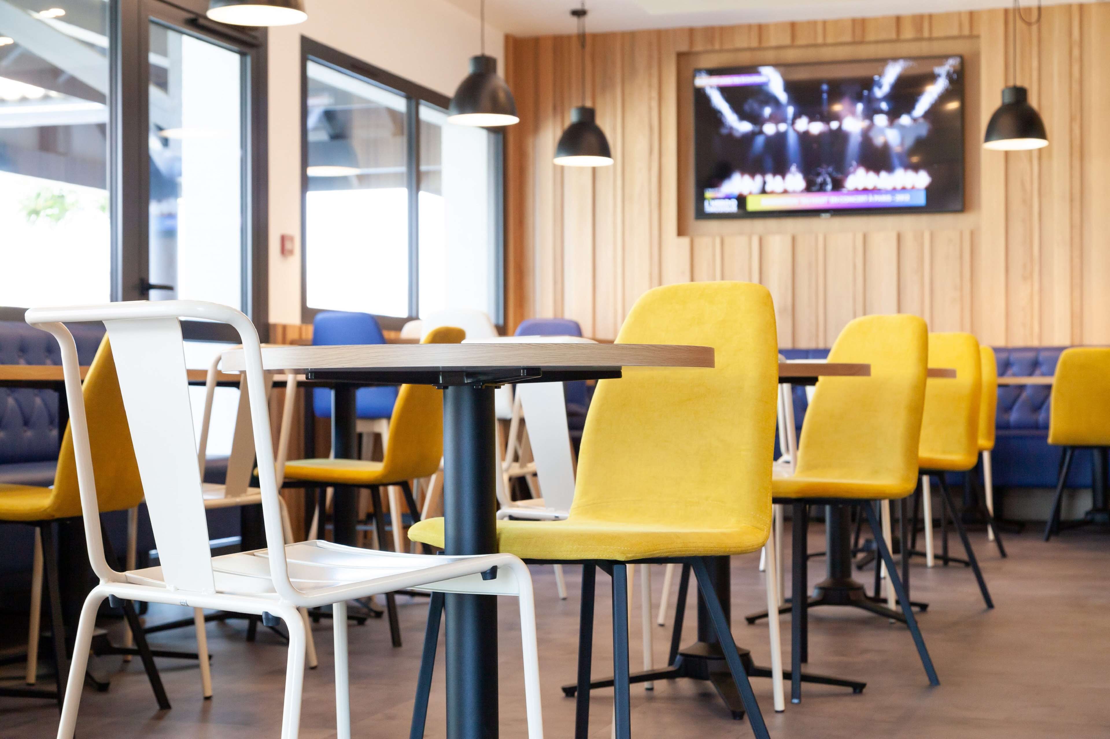 Un comedor moderno con sillas amarillas y blancas, mesas de madera e iluminación colgante.