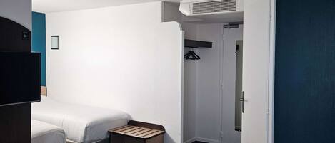 Una habitación de hotel con dos camas, un televisor, un armario y una mesita.