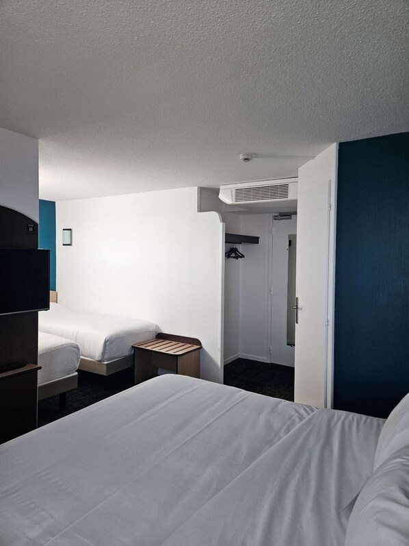 Une chambre d’hôtel avec deux lits, une télévision, une armoire et une petite table.