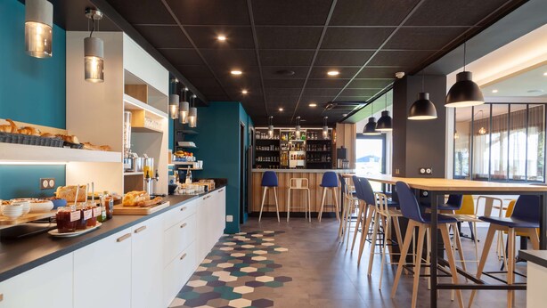Una cafetería moderna con un mostrador central, zona de bar y mesas.