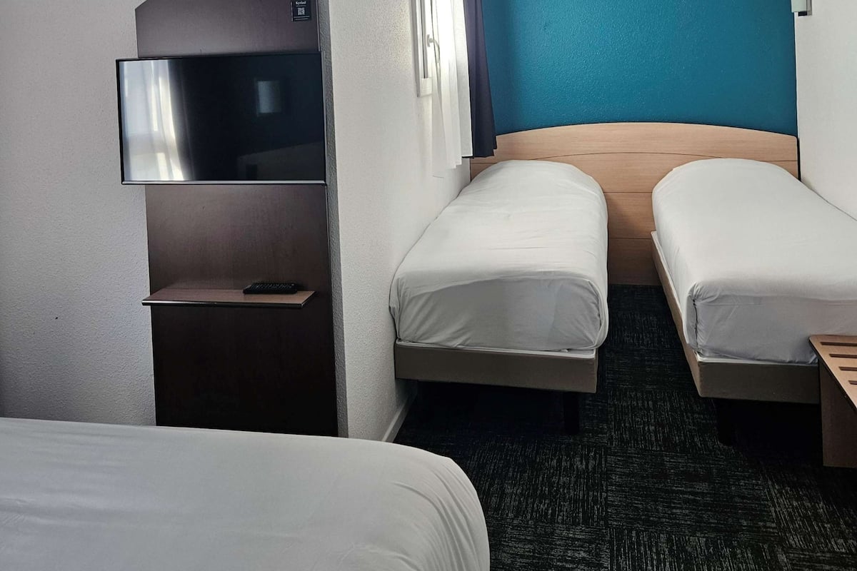 Une chambre d’hôtel avec deux lits simples, un téléviseur à écran plat fixé au mur et une tête de lit en bois.