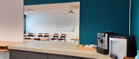 Un salón de conferencias con una gran mesa, sillas, una pizarra y una máquina de café.
