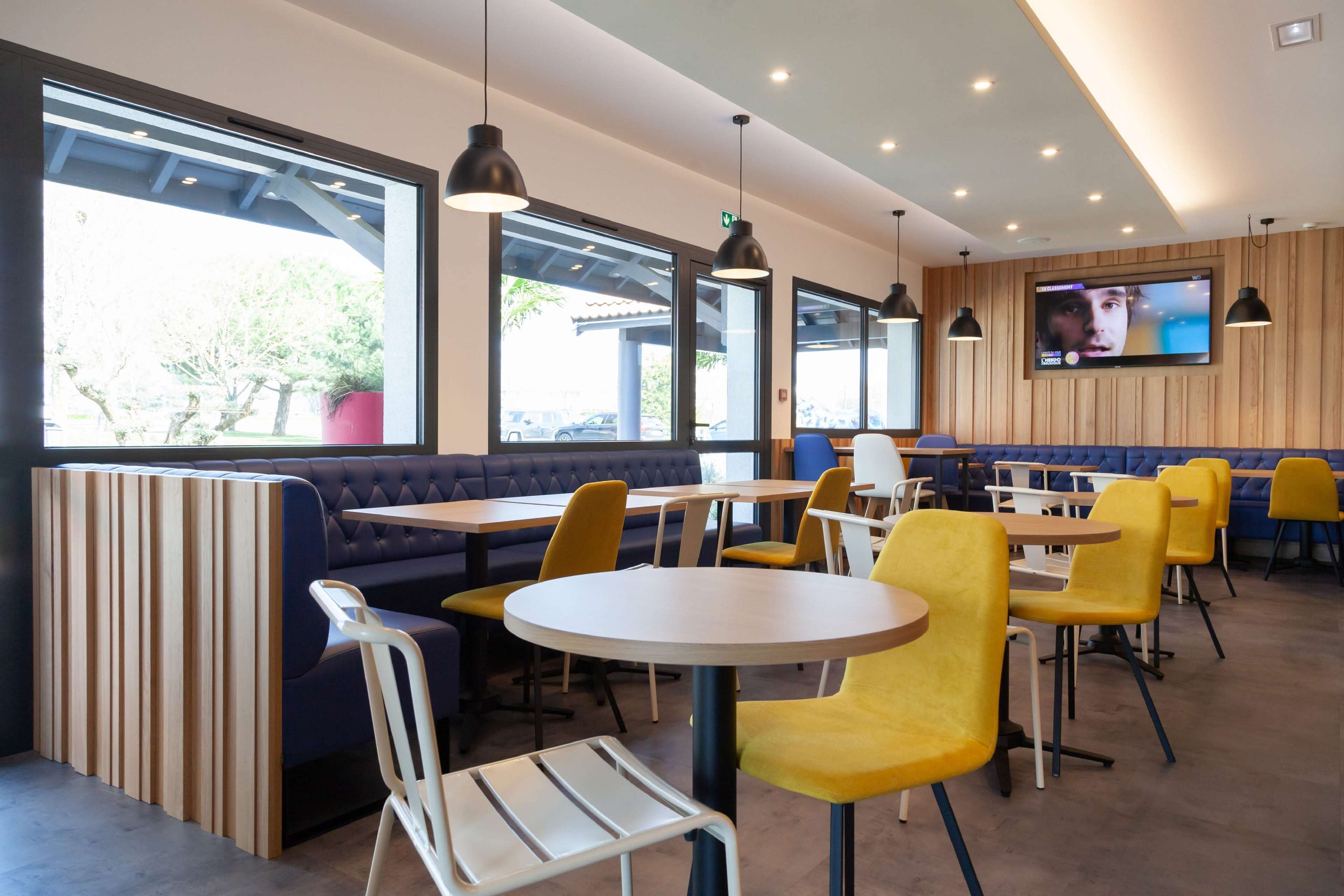 Un restaurant moderne avec des banquettes, des tables rondes et des chaises jaunes.