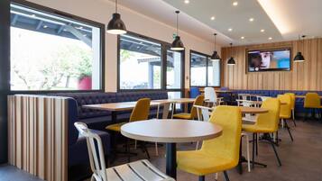 Un restaurant moderne avec des banquettes, des tables rondes et des chaises jaunes.