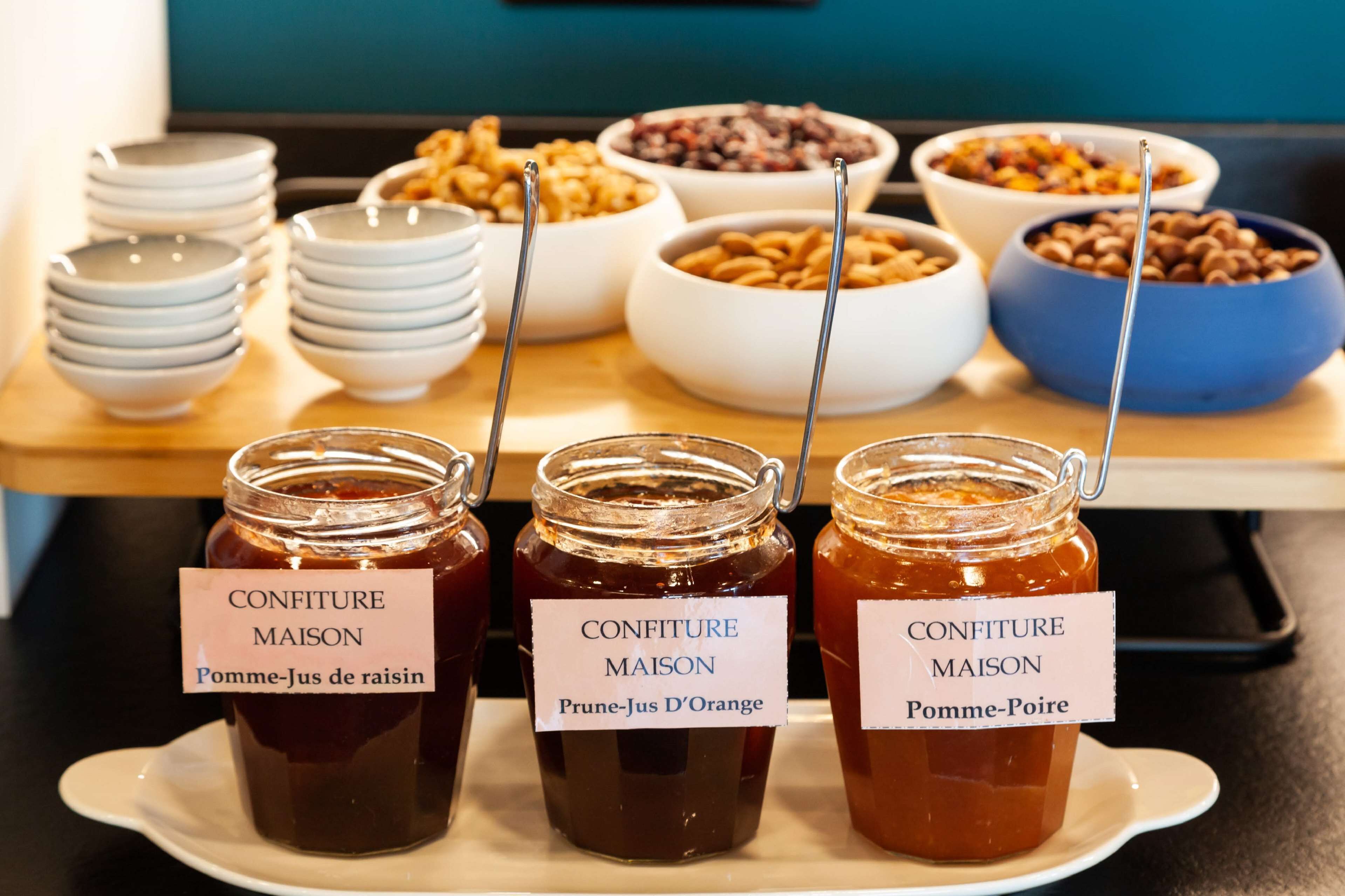 Una mesa de buffet con diversos alimentos y tres frascos de mermelada etiquetados con distintos nombres de frutas.