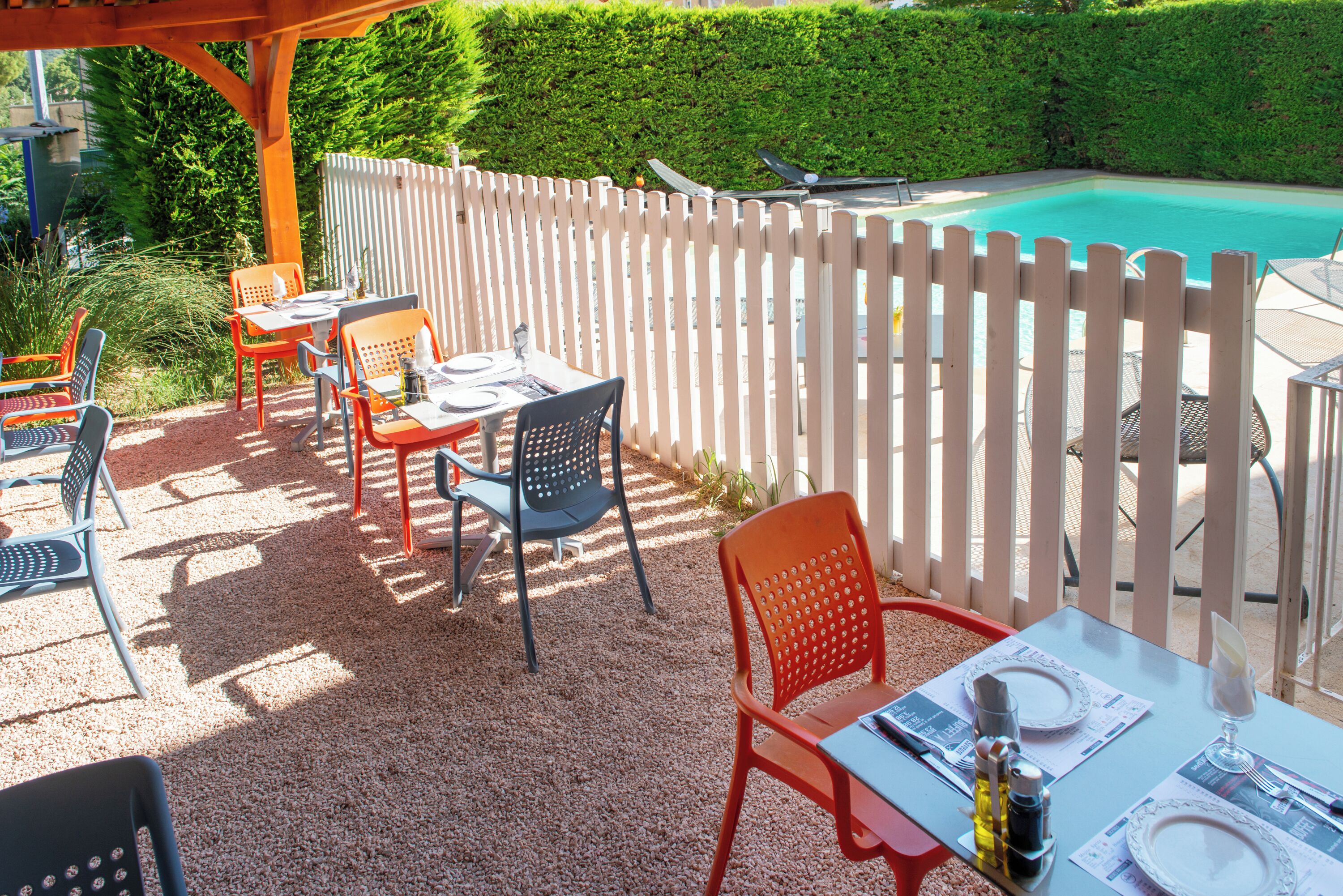 Eine Terrasse im Freien mit Tischen und Stühlen, einem Pool und einem weißen Zaun.