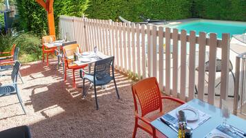 Eine Terrasse im Freien mit Tischen und Stühlen, einem Pool und einem weißen Zaun.