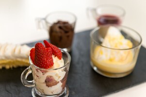 Un vassoio con diversi dessert, tra cui un bicchiere con fragole e panna montata, un bicchiere con mousse al cioccolato e un bicchiere con un dessert giallo.