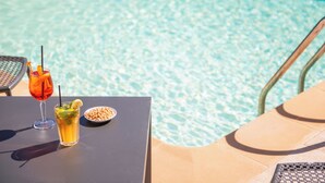 Mesa junto a la piscina con una bebida y un tazón de nueces.