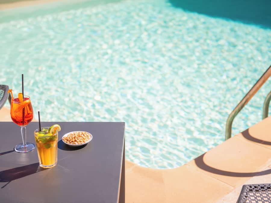 Mesa junto a la piscina con una bebida y un tazón de nueces.
