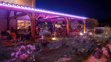 Un espace de restauration en plein air agrémenté de pergolas et de tables en bois, entouré de jardins aménagés et de plantes décoratives.