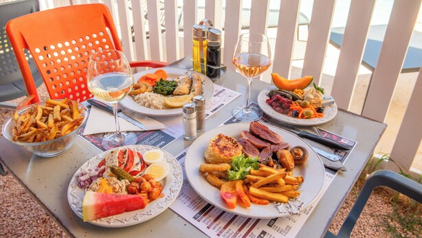 Una mesa servida con varios platos, entre ellos mariscos, filete y papas fritas, con una vista a una piscina al fondo.