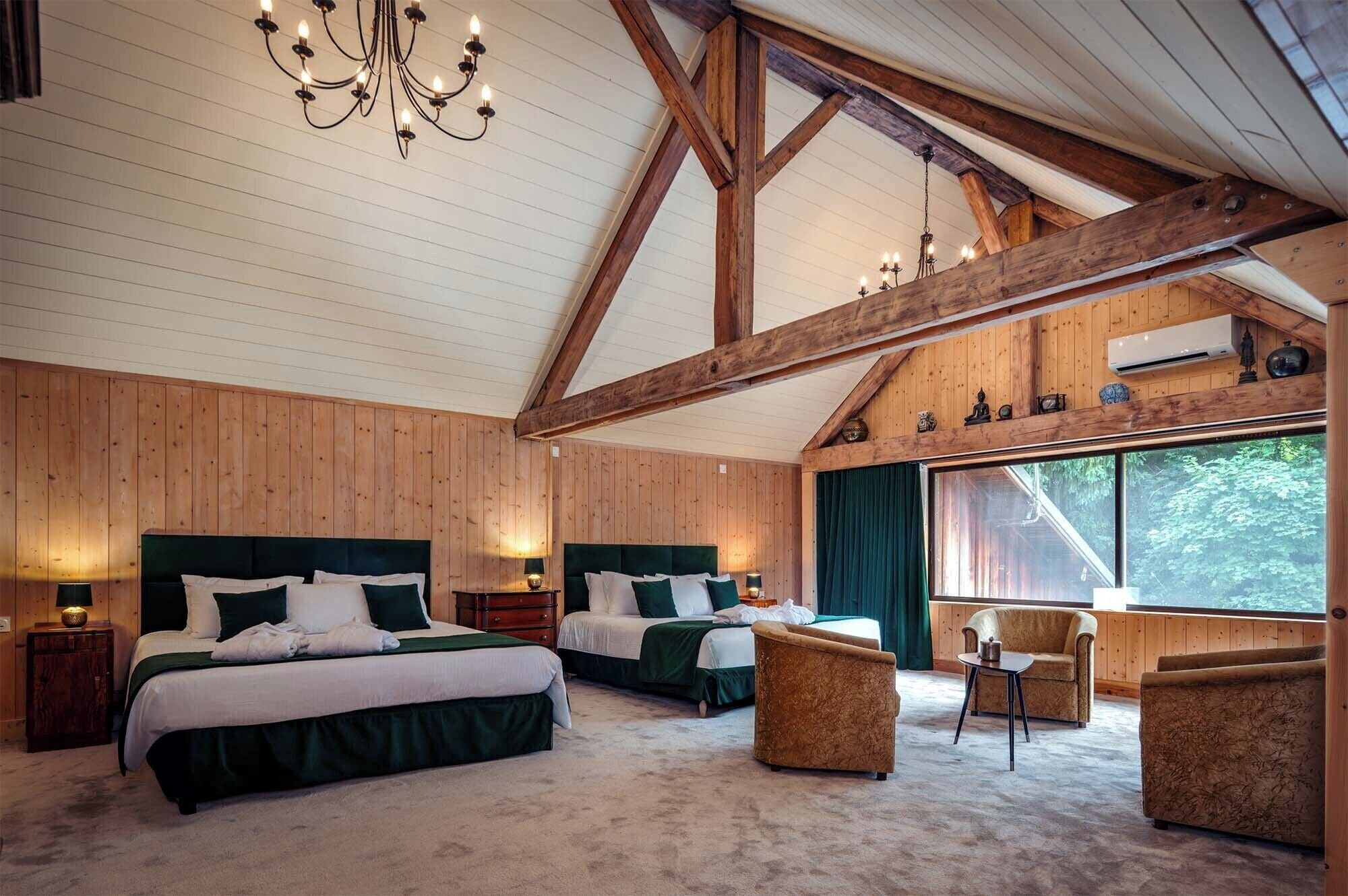 A spacious bedroom with two beds, a chandelier, wooden beams, a large window with a view, and a cozy seating area.