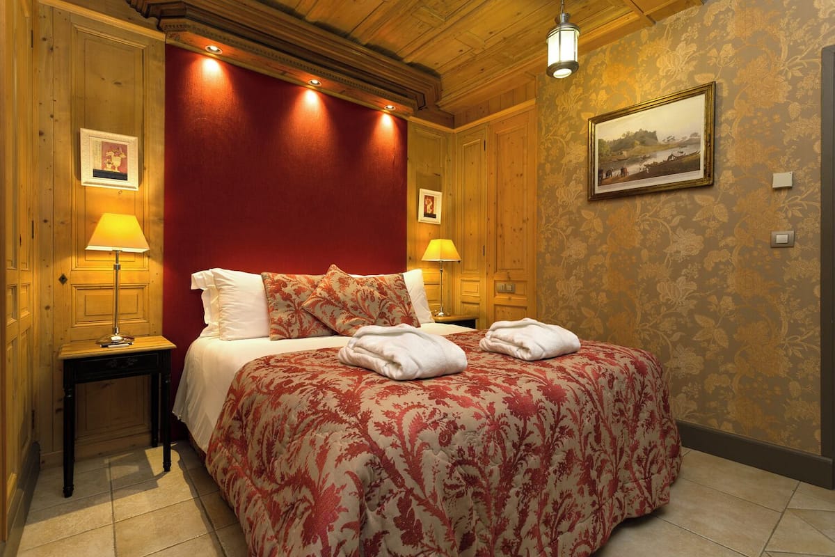 Habitación de hotel con techo de madera, una pared de acento roja, cama con ropa de cama floral, dos lámparas de noche y un cuadro enmarcado en la pared.