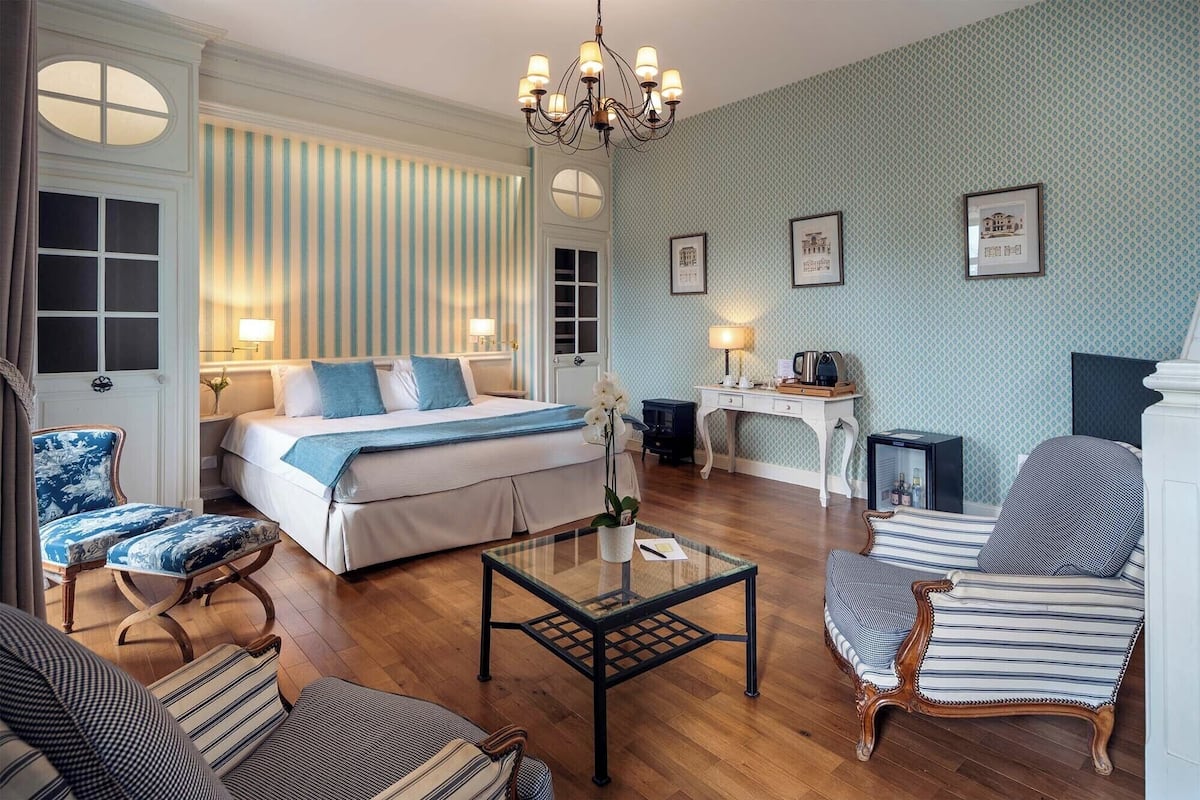 Habitación de hotel con una cama grande, dos sillones, una mesita y un escritorio con lámpara.