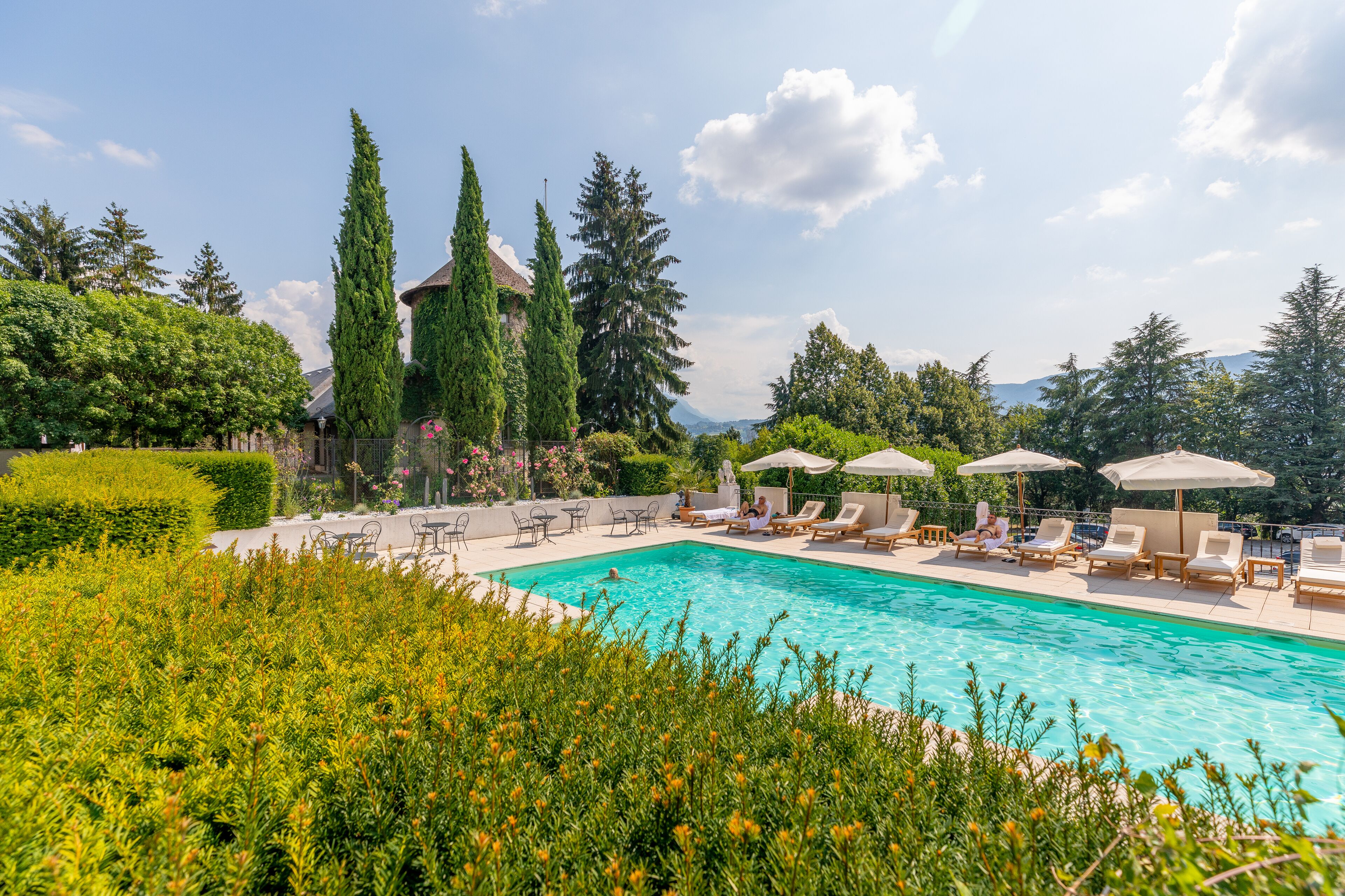 A swimming pool with lounge chairs and umbrellas, surrounded by greenery and trees.