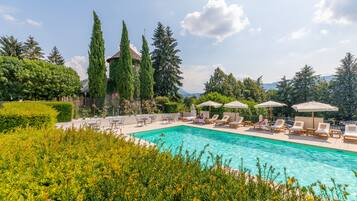 A swimming pool with lounge chairs and umbrellas, surrounded by greenery and trees.