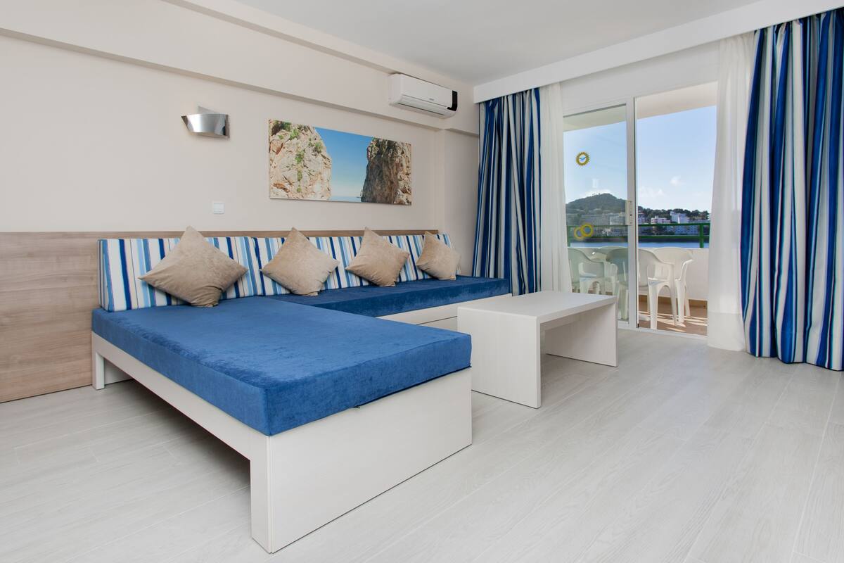 Ein modernes Hotelzimmer mit einem großen Bett, einer kleinen Couch, einer Bank und einem Balkon mit Meerblick.
