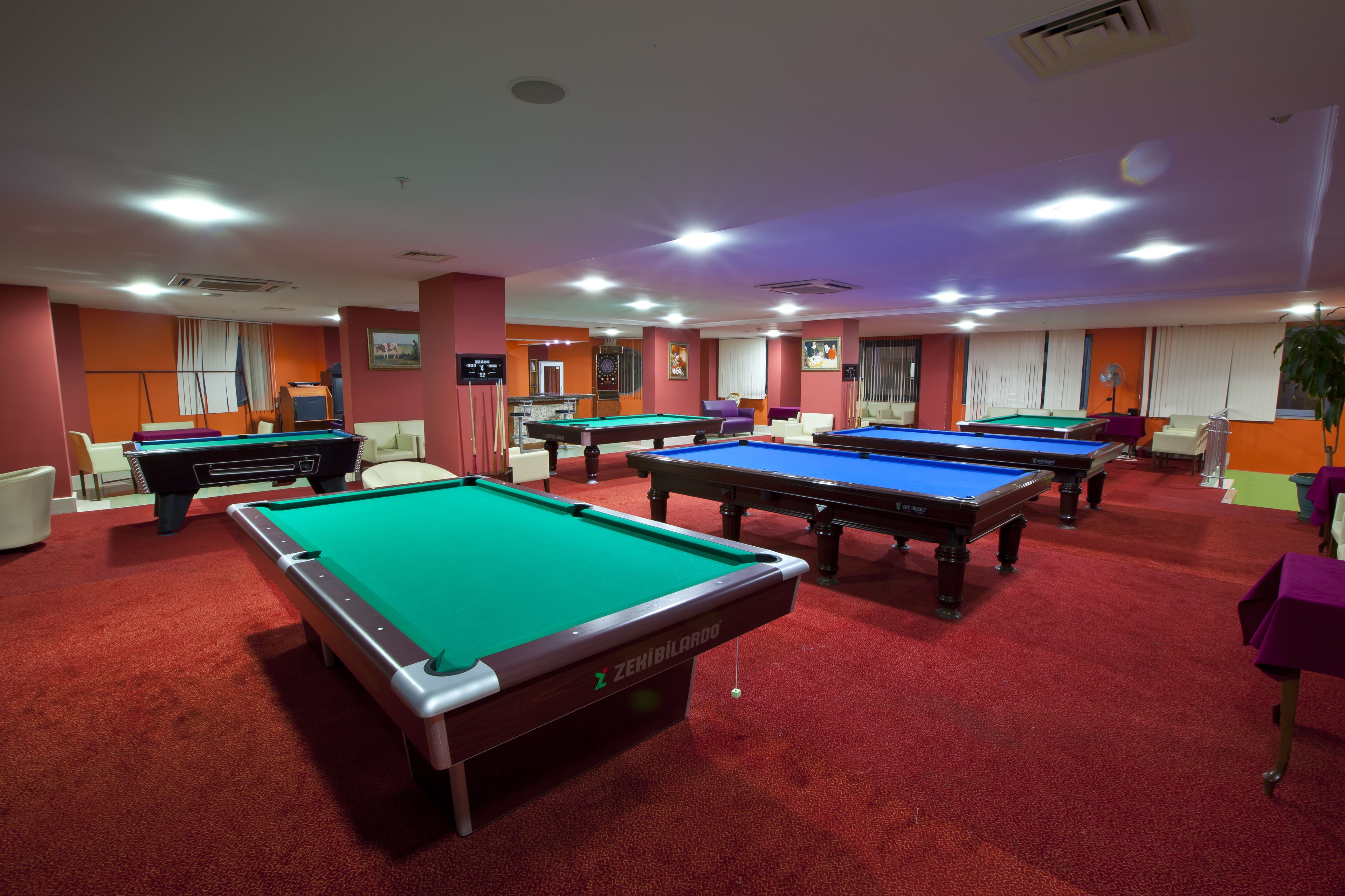 A pool hall with multiple pool tables, red carpet flooring, and orange walls.