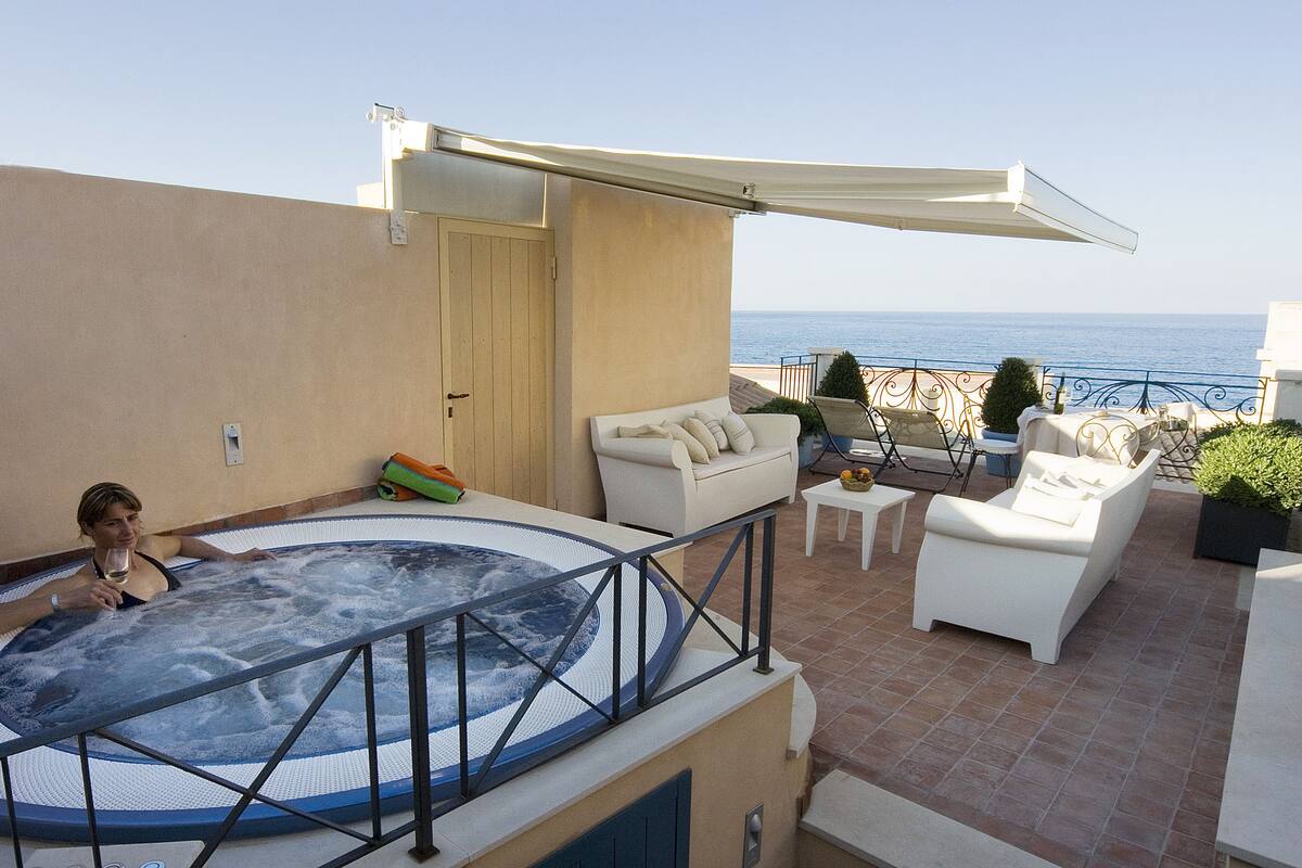 Una terraza en la azotea con jacuzzi, mobiliario exterior y vistas al mar.