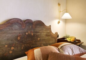 Un cabecero de madera con un diseño único, una mesita de noche con fruteros y una lámpara fijada a la pared.