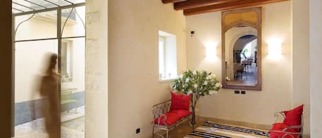 Una habitación con techo de madera, alfombra a rayas, dos sillas de mimbre con cojines rojos y un espejo en la pared.