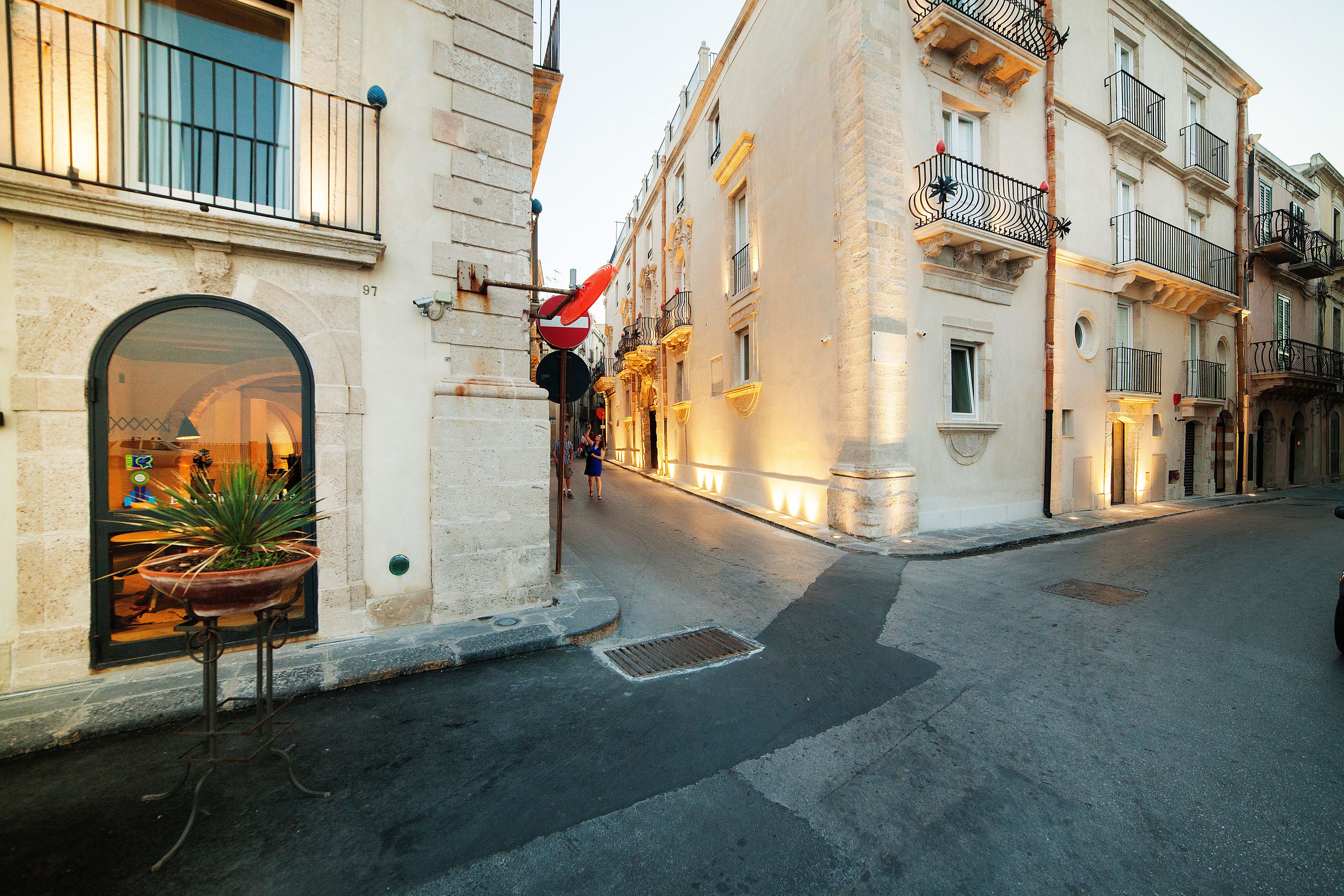 A street with buildings, a potted plant, and a red and black sign.