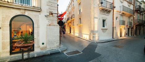 A street with buildings, a potted plant, and a red and black sign.