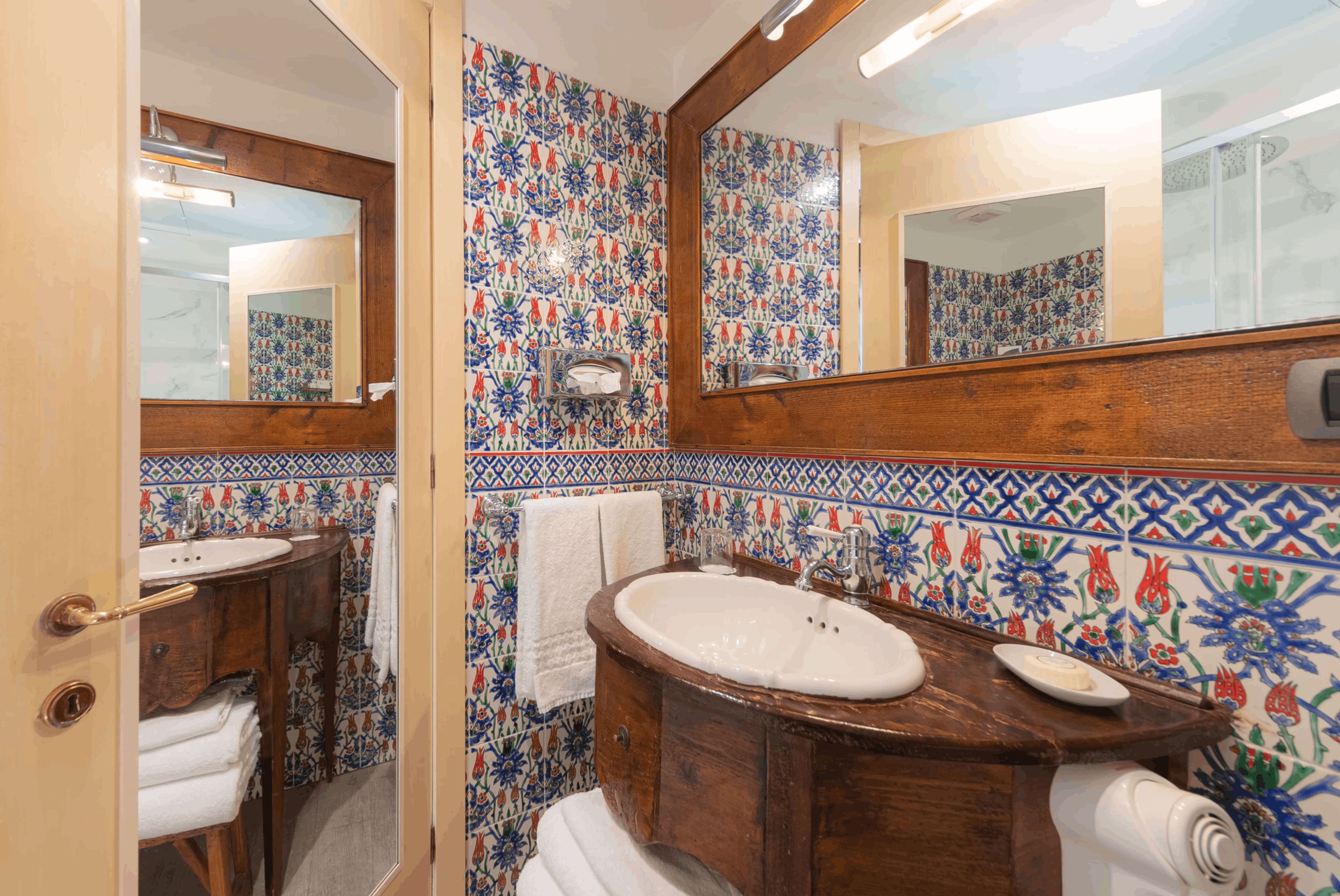 A bathroom with a wooden vanity, a mirror, and a tiled wall with floral patterns.