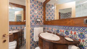 A bathroom with a wooden vanity, a mirror, and a tiled wall with floral patterns.