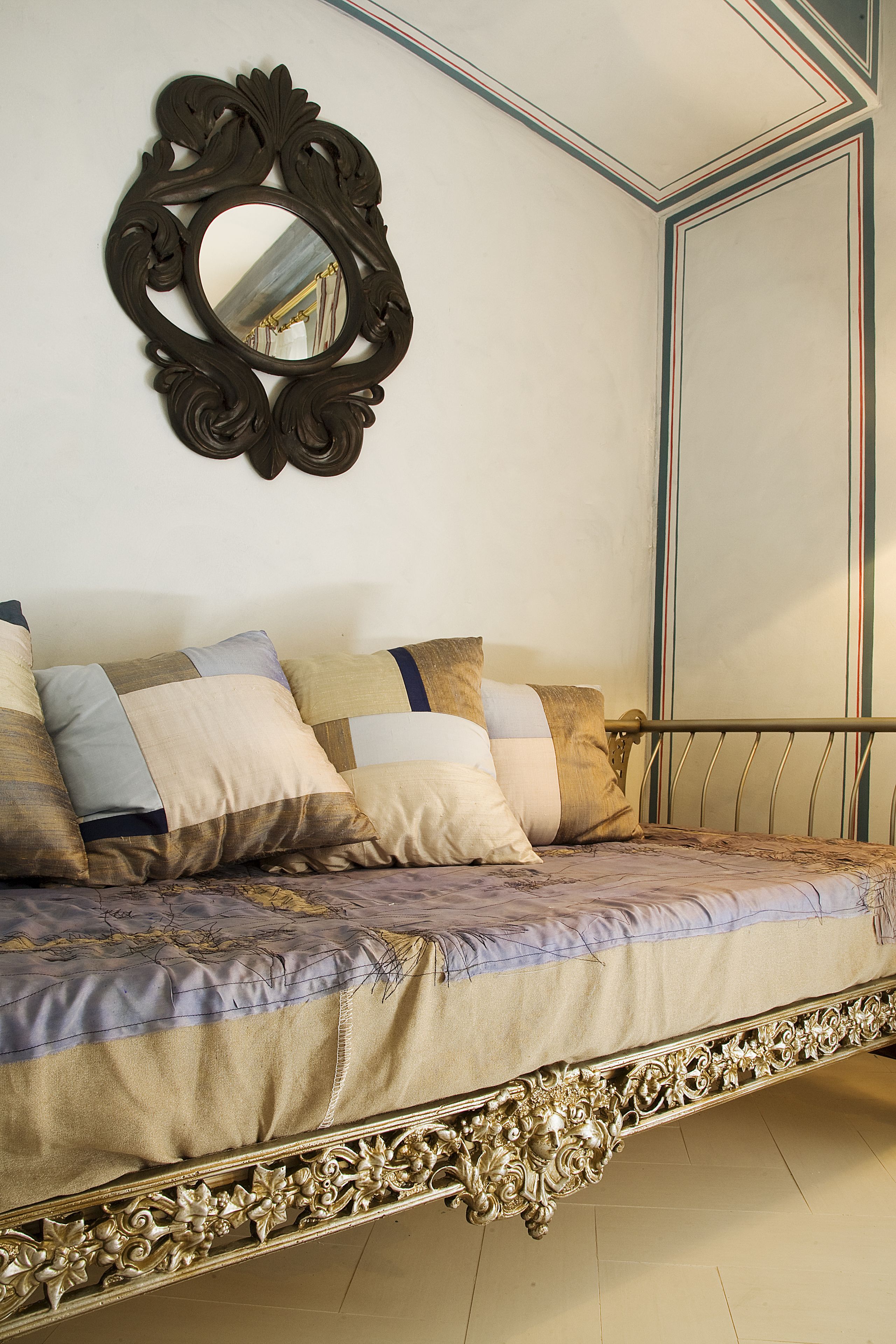 Una cama con un cabecero decorado, un espejo y una pared a rayas.