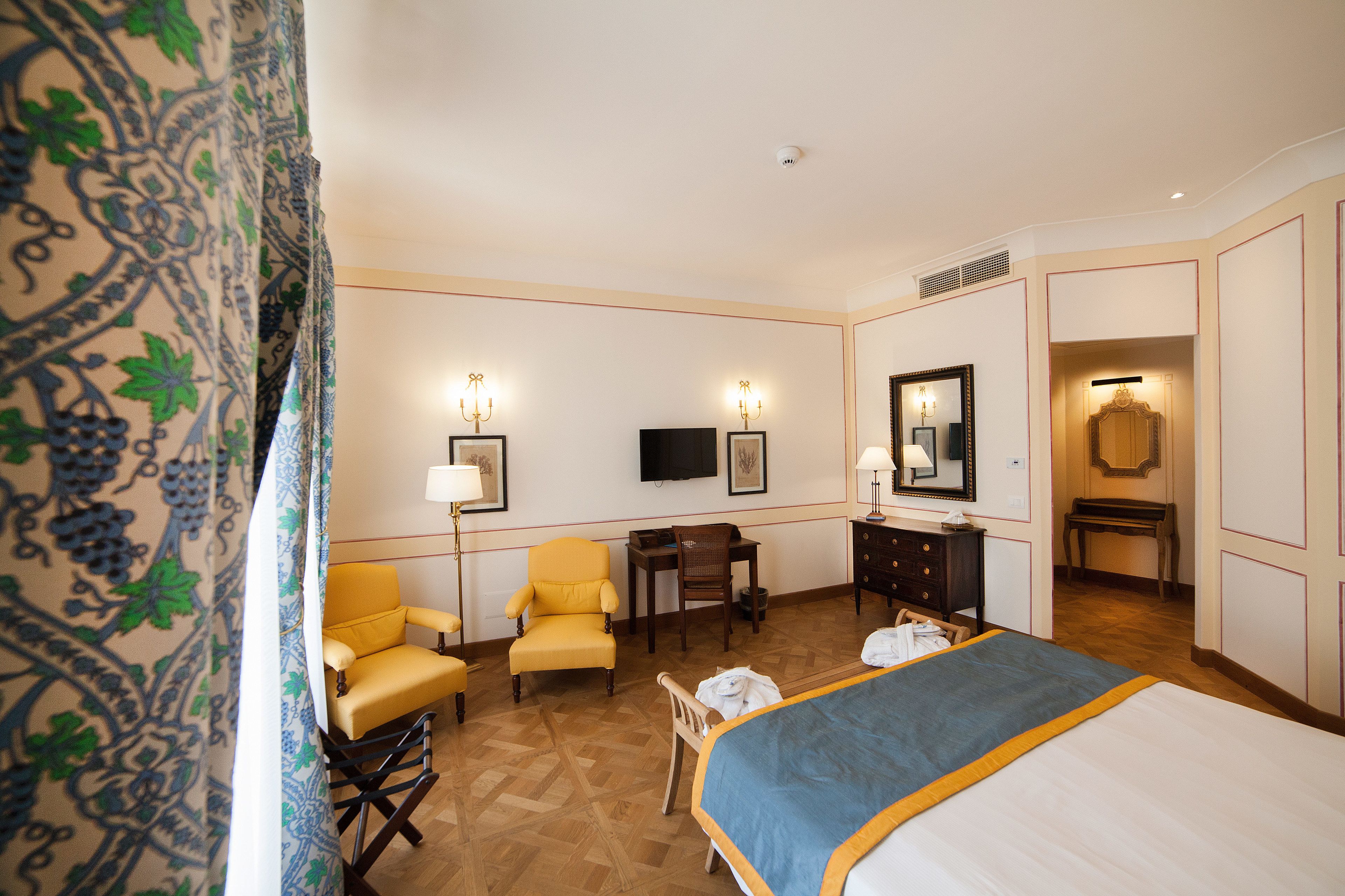 A hotel room with a bed, a desk, two chairs, a dresser, a television, and a mirror.