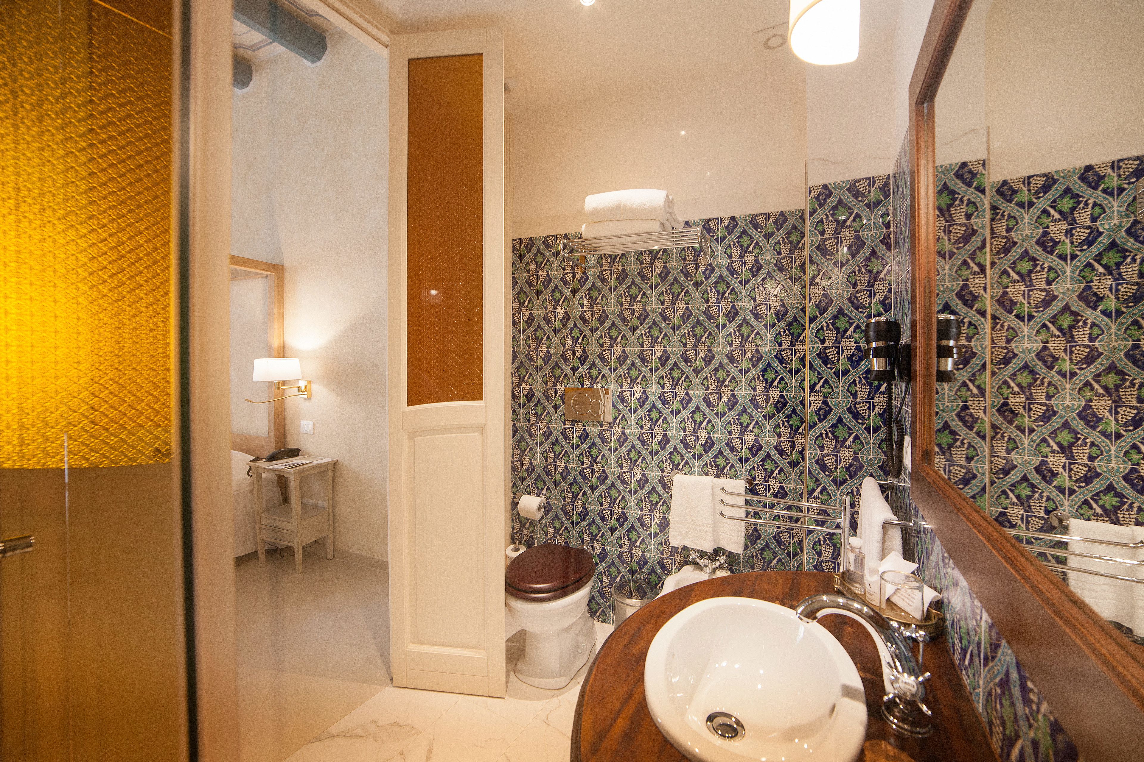 Een badkamer met een betegelde muur, een houten wastafelmeubel, een wastafel en een toilet.