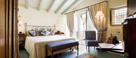 A bedroom with a bed, bedside table, chair, desk, lamp, and a view of the outdoors.