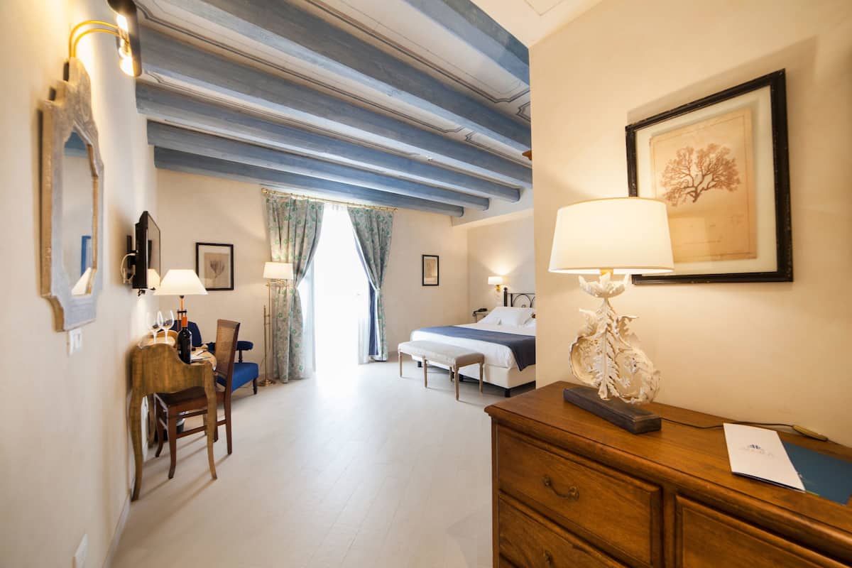 Una habitación de hotel con cama, mesita de noche, lámpara, sillón y escritorio con lámpara.
